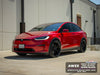 A red Tesla Model Y with custom black wheels and a glossy black wrap, parked outdoors in front of a beige building.