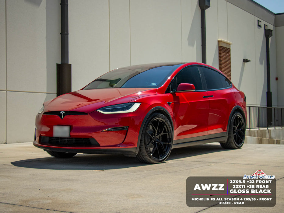 A red Tesla Model Y with custom black wheels and a glossy black wrap, parked outdoors in front of a beige building.